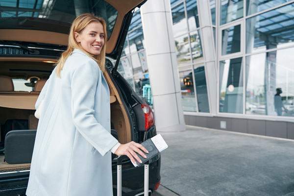 cheerful woman getting luggage out of taxi, heading into airport with boarding pass