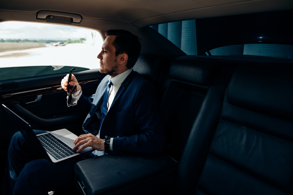 business man in executive class taxi, working on laptop in suit