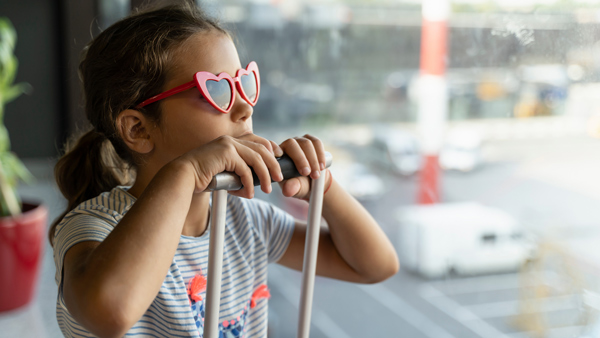 young girl with heart sunglasses, sitting on suitcase in airport